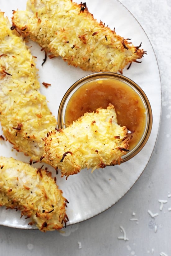 Baked Coconut Chicken Tenders on a plate with one dunked in sauce.