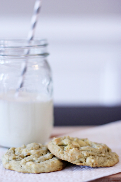 Two Pistachio White Chocolate Chip Cookies on a napkin with a glass of milk.