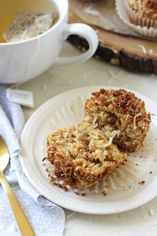 A split open Coconut Streusel Muffin on a plate with a cup of tea.