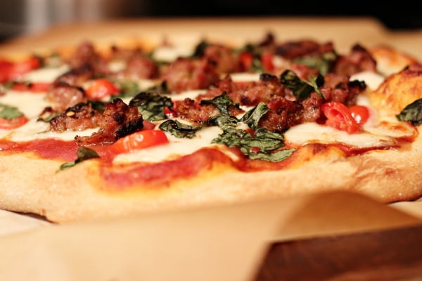 A Sausage, Mozzarella and Basil Pizza on a wooden pizza peel.