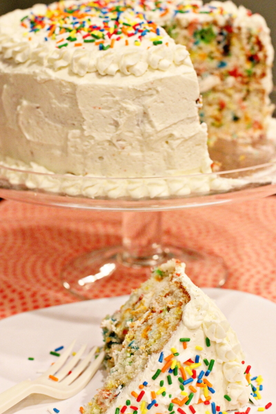 A slice of Layered Funfetti Cake with the full cake in the background.