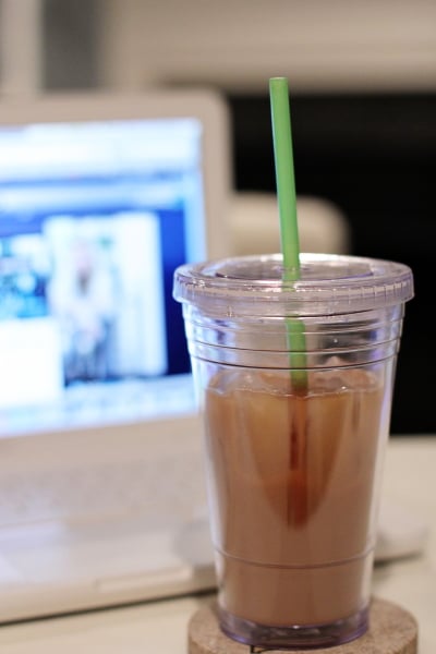 A DIY Iced Coffee in a travel cup in front of a computer.