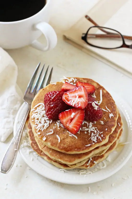 Several Macadamia Nut Pancakes on a plate with a cup of coffee to the side.