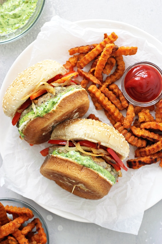 Two Pesto Turkey Burgers on a white plate with sweet potato fries and ketchup.