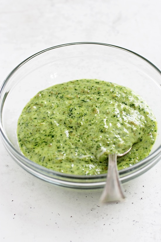 A glass mixing bowl filled with Pesto Mayo with a spoon in the dish.
