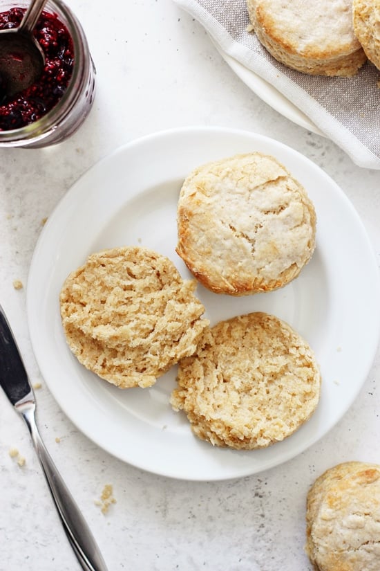 Two Coconut Oil Biscuits on a white plate with one split in half and jam to the side.