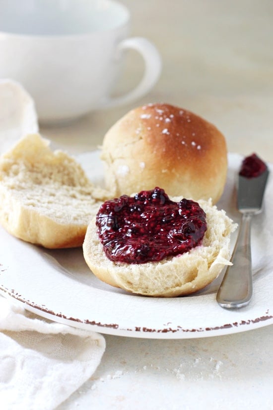 A Honey Dinner Roll split open on a plate and slathered with jam.