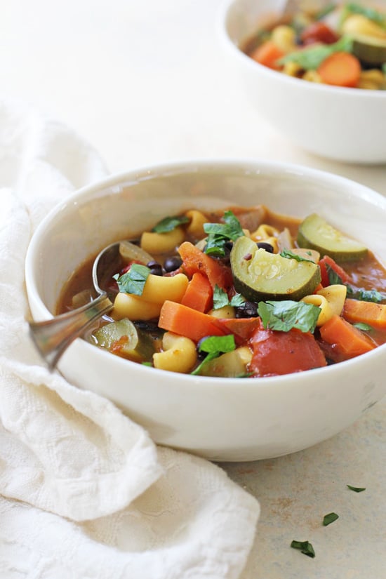 A white bowl filled with Vegan Minestrone Soup with a spoon in the dish.