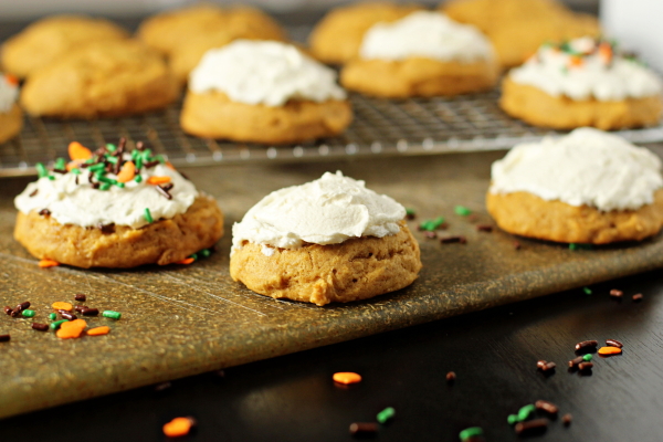 Several Pumpkin Cookies with Maple Frosting on a cutting board and cooling rack.