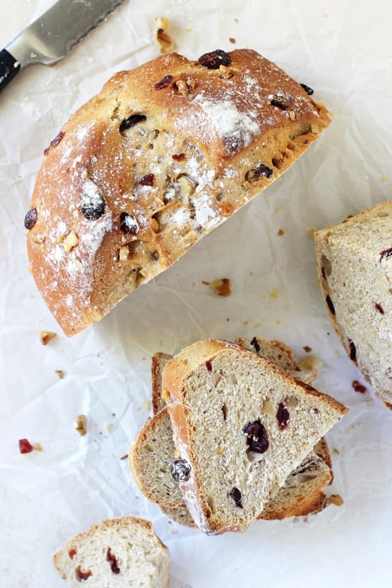 A sliced up loaf of Cranberry Walnut Yeast Bread on parchment paper.