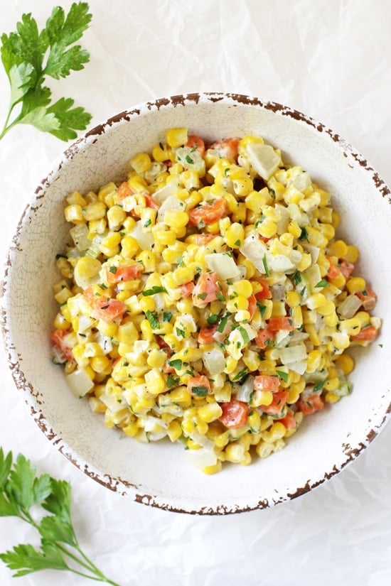 A white bowl filled with Holiday Corn and fresh parsley to the side.