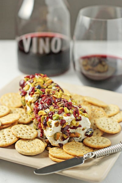 A Baked Goat Cheese Log on a platter coated with cranberries and pistachios.