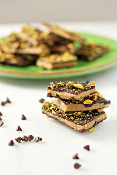 Three stacked pieces of Dark Chocolate Pistachio Toffee with more in the background.