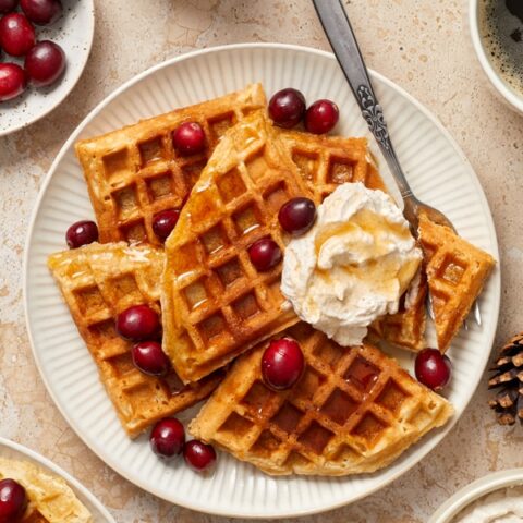 Eggnog Waffles on a plate with cranberries and whipped cream.