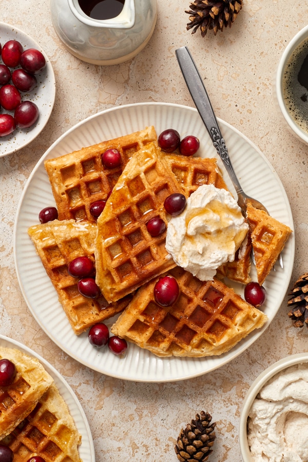 Eggnog Waffles on a plate with cranberries and whipped cream.