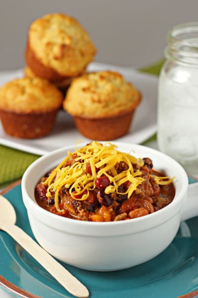 A white bowl filled with Sausage and Beef Chili with cornbread in the background.