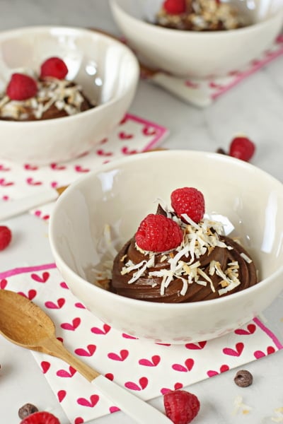 A white bowl filled with Chocolate Avocado Mousse topped with raspberries.