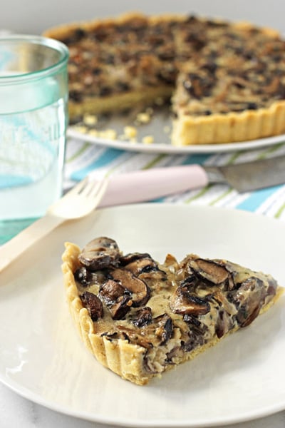 A slice of Wild Mushroom Tart on a plate with a glass of water to the side.