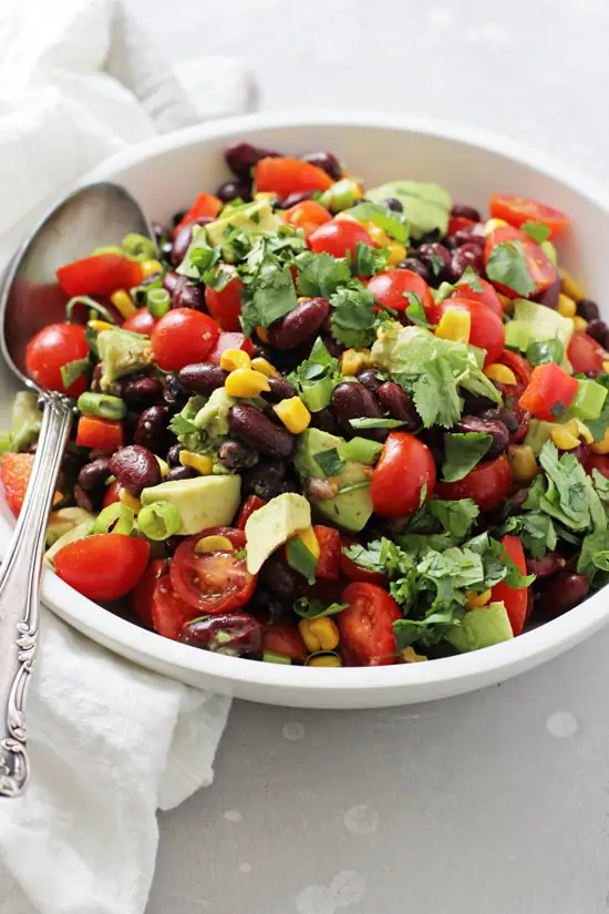 A white bowl filled with Mexican Bean Salad with a silver spoon in the bowl.