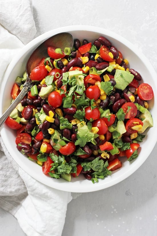 A white bowl filled with Mexican Black Bean Salad with a silver serving spoon in the dish.