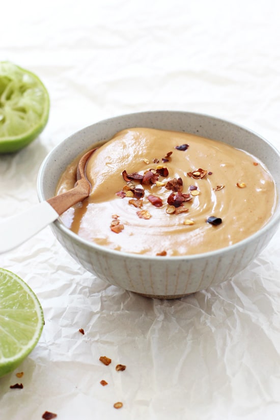 A grey bowl filled with Homemade Peanut Sauce with limes to the side.