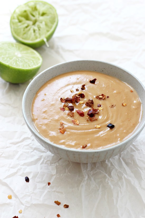 A grey bowl filled with Homemade Thai Peanut Sauce with lime halves in the background.