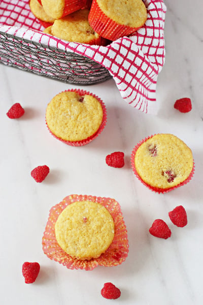 Several Raspberry Corn Muffins in a basket and on a marble surface.