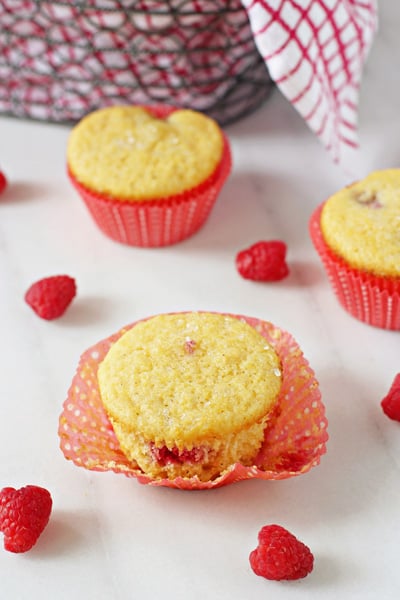An unwrapped Raspberry Cornbread muffin on a marble surface with fresh raspberries.