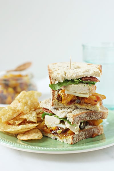 A stacked Chicken and Chutney Sandwich on a plate with chips.