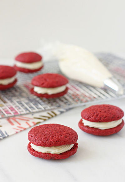 Several Red Velvet Sandwich Cookies and a piping bag of frosting.