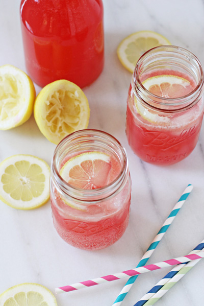 Two glasses of Sparkling Raspberry Lemonade with lemon slices and straws.