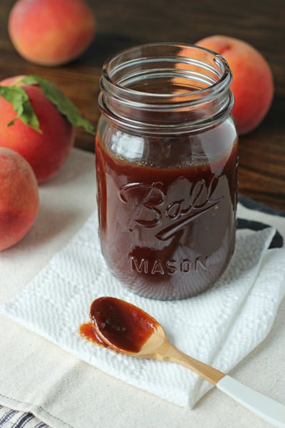 A jar of Peach BBQ Sauce with some taken out with a spoon.