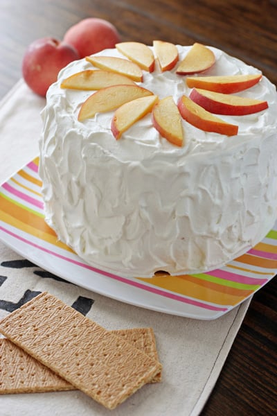 A Graham Cracker Cake on a colorful platter topped with fresh peaches.