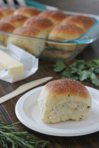 A Herb Yeast Roll on a white plate with more in a baking dish.