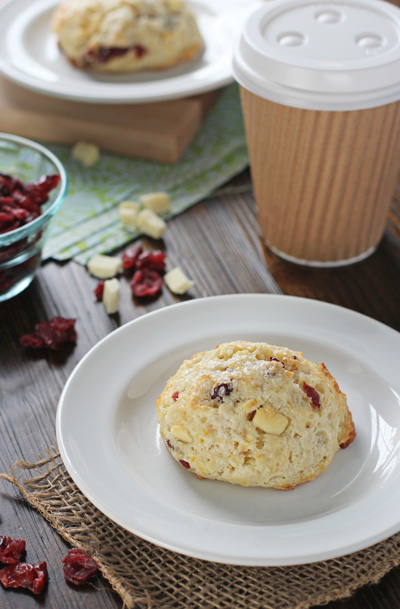 A Cranberry and White Chocolate Scone on a plate with coffee to the side.
