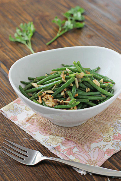 A white serving bowl filled with Green Beans with Almonds and Shallots.