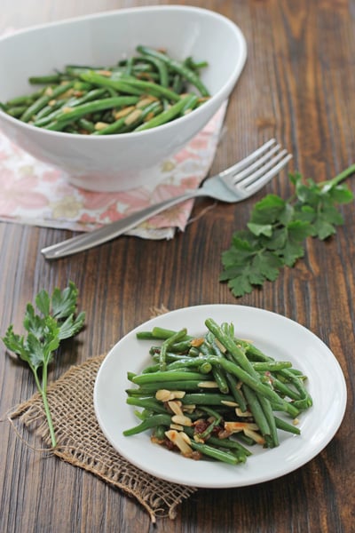 A white plate and serving bowl filled with Green Beans with Almonds.