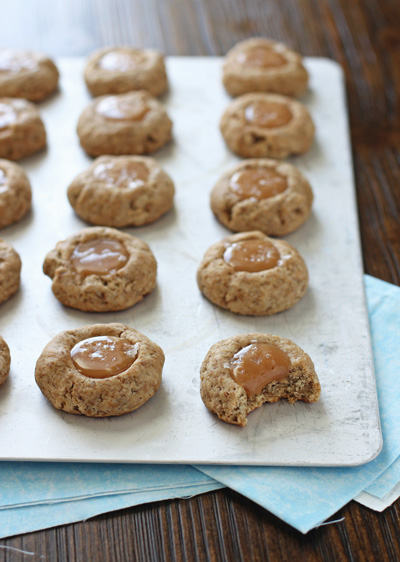 A baking sheet with Salted Caramel Thumbprint Cookies with a bite taken out of one.