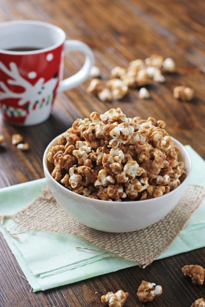 A bowl filled with Gingerbread Caramel Corn and a cup of coffee.