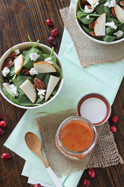 A jar of Cranberry Vinaigrette with two salads to the side.