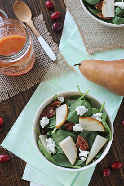 A Winter Spinach Salad in a white bowl with cranberry dressing to the side.