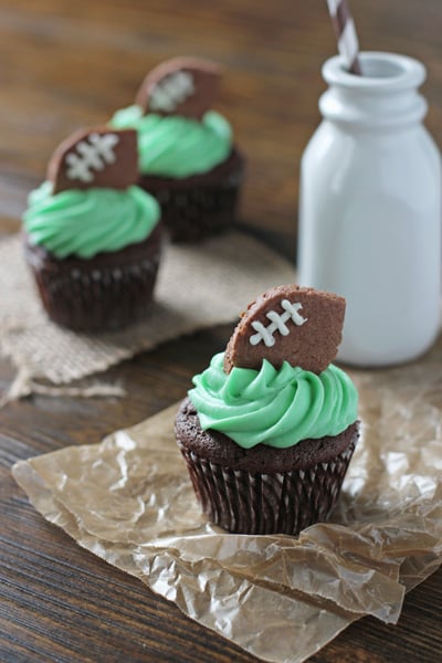 Three Football Cupcakes on wax paper with a jug of milk.