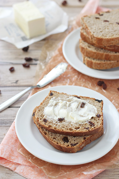 Two slices of Whole Wheat Cinnamon Raisin Bread on a plate with one buttered.