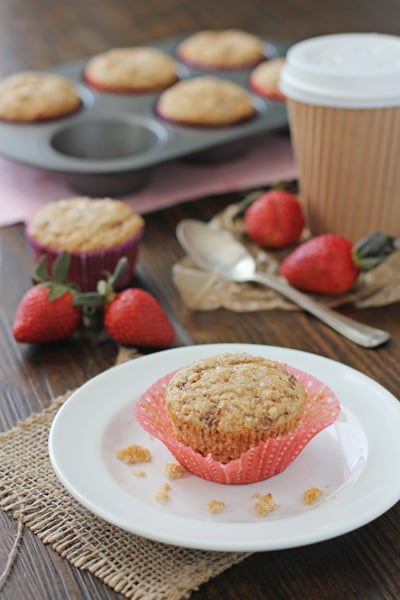 An unwrapped Fresh Strawberry Muffin on a plate with crumbs.