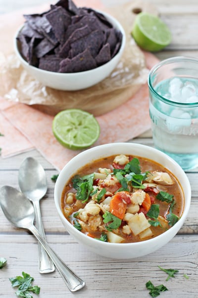 A bowl of Chipotle Chicken Soup with chips and limes to the side.