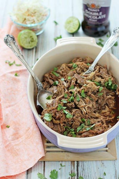 A baking dish filled with Slow Cooker Beer Pulled Pork with serving spoons in the dish.