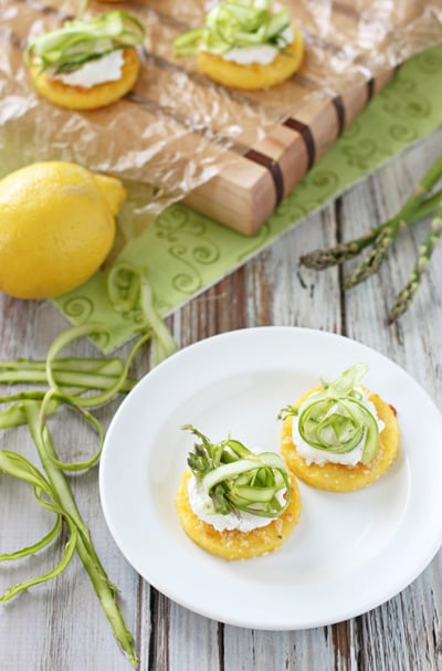 Two Polenta Cakes on a white plate topped with ricotta and asparagus.