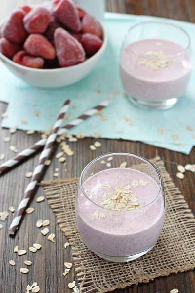 A glass filled with Strawberry Oatmeal Smoothie with frozen berries to the side.