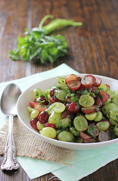 A white bowl filled with Fruit Salsa with Grapes with a spoon to the side.