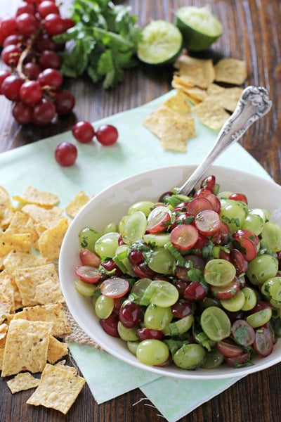 A white bowl filled with Grape Salsa and chips to the side.